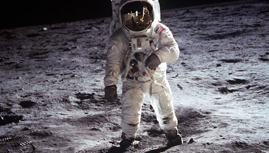 Astronaut Buzz Aldrin steht auf der staubigen Oberfläche des Monds. Er trägt einen weißen Raumanzug mit einem Helm.