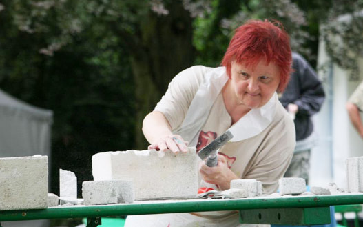 Eine Frau mit roten Haaren in einem weißen Overall arbeitet mit einem Bildhauerhammer an einem weißen Betonstein
